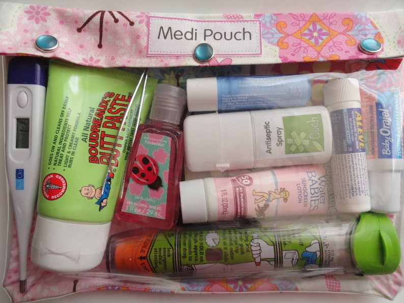 May include: A pink fabric pouch with the words "Medi Pouch" printed on it. The pouch contains a variety of items, including a thermometer, a tube of diaper rash cream, a bottle of hand sanitizer, a tube of sunscreen, a tube of lip balm, a tube of pain relief cream, and a small bottle of antiseptic spray.