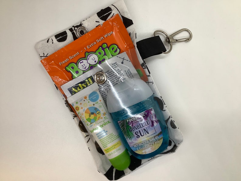 May include: A clear plastic pouch with a black and white patterned fabric exterior. The pouch contains a small bottle of hand sanitizer, a tube of sunscreen, a tube of lip balm, and a small packet of Boogie wipes. The pouch has a black strap with a silver clip.