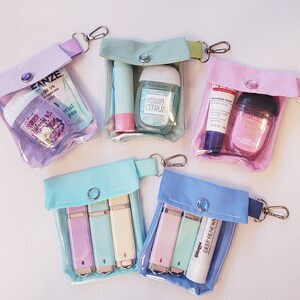 May include: Five clear plastic zippered pouches with different colored fabric exteriors. Each pouch contains various small items, including hand sanitizer, lip balm, and small tubes. The pouches have a zipper closure and a metal ring for attaching to a keychain.