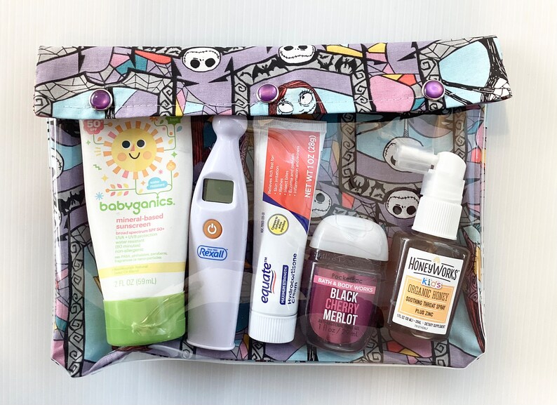 May include: A clear zippered pouch with a colorful Nightmare Before Christmas print. The pouch contains a variety of items, including sunscreen, a thermometer, hand sanitizer, a tube of cream, and a nasal spray.