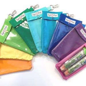 Puede incluir: Una colección de estuches EpiPen coloridos en varios tonos, desde naranja hasta morado. Cada estuche tiene una parte delantera transparente, un cierre a presión y un mosquetón plateado. El logotipo de EpiPen es visible en cada estuche.