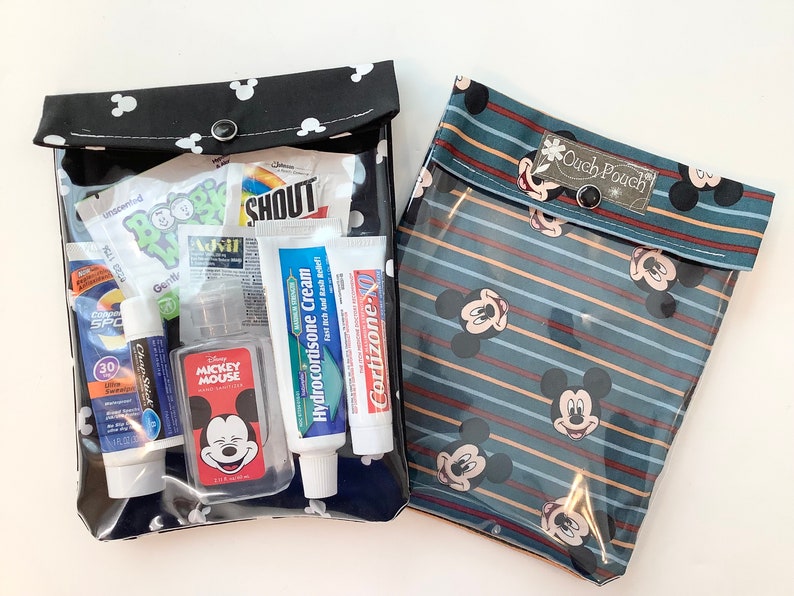 May include: Two clear plastic zippered pouches with Mickey Mouse patterns. The black pouch has white polka dots and contains various toiletries, including sunscreen, hand sanitizer, and lip balm. The blue pouch has red and white stripes and the text "Ouch Pouch".