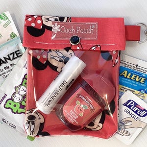 May include: Red zippered pouch with a clear plastic window, featuring a Mickey Mouse design. The pouch contains various items, including hand sanitizer, pain relief tablets, and a small tube of hand cream. The pouch has a red strap with a silver carabiner clip.