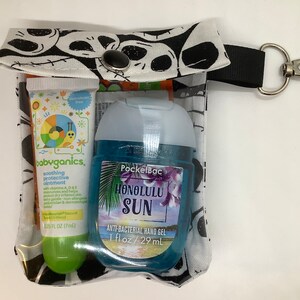 May include: A clear plastic zippered pouch with a black and white skull print. The pouch contains a small green and white tube of babyganics soothing protective ointment and a blue bottle of PocketBac Honolulu Sun anti-bacterial hand gel. The pouch has a black strap with a silver clip.