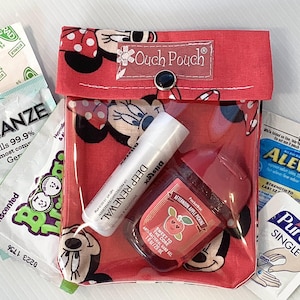 Könnte beinhalten: Eine rote und weiße Mickey-Mouse-Tasche mit einem transparenten Plastikfenster. Die Tasche enthält verschiedene Artikel, darunter Händedesinfektionsmittel, Lippenbalsam und eine kleine Flasche Handlotion. Die Tasche hat einen Knopfverschluss und der Text "Ouch Pouch" ist auf der Vorderseite aufgedruckt.