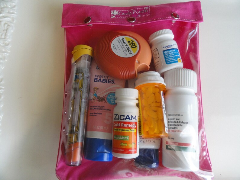 May include: A clear, pink, zippered pouch labeled "Cach Pouch" containing various medications. Items include an inhaler, a pre-filled epinephrine auto-injector, bottles of pills, and a tube of sunscreen. The pouch is closed with snaps.