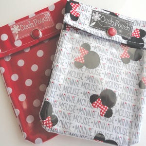 Puede incluir: Dos bolsas de tela. Una es roja con lunares blancos. La otra es blanca con siluetas grises de Minnie Mouse y las palabras "MINNIE MOUSE" repetidas. Ambas tienen un cierre de botón a presión rojo y el texto "Ouch Pouch".