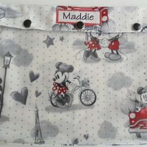 May include: A white fabric zipper pouch with a gray polka dot pattern. The pouch features a Mickey Mouse and Minnie Mouse design with red, black, and white accents. The pouch has a flap with a personalized name tag that reads "Maddie".