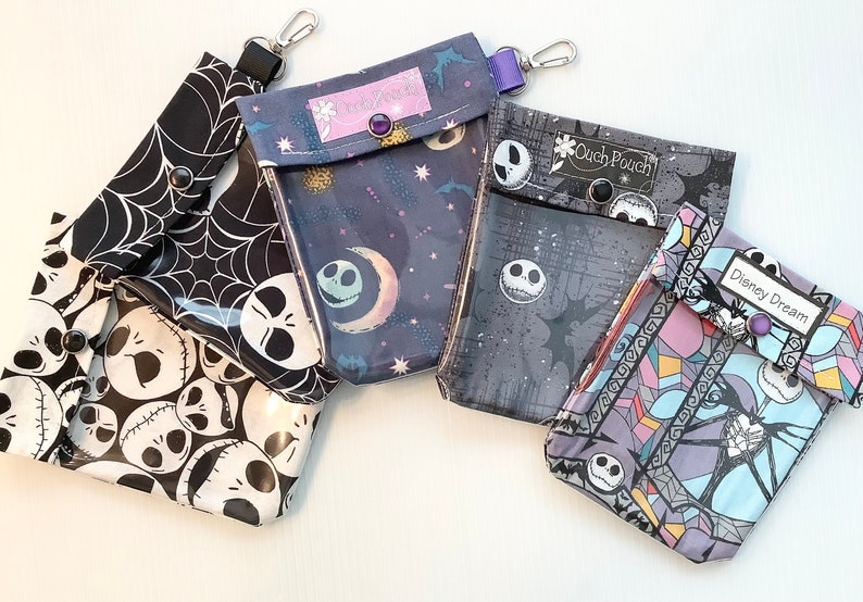 Puede incluir: Cuatro bolsas de tela diferentes con una ventana de pl&aacute;stico transparente. Cada bolsa presenta un dise&ntilde;o diferente con un personaje de Jack Skellington en blanco y negro de la pel&iacute;cula Pesadilla antes de Navidad. Las bolsas tienen una correa morada y un cierre de metal. El texto en las bolsas dice "Ouch Pouch", "Disney Dream" y "The Pumpkin King".