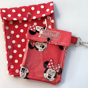 Könnte beinhalten: Zwei rote und weiße gepunktete Beutel mit klaren Vinylfenstern. Der kleinere Beutel hat ein Mickey-Mouse-Charakterdesign und den Text "Ouch Pouch" auf der Vorderseite. Der größere Beutel hat einen Reißverschluss und ein weißes Punktmuster.