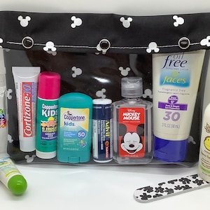 May include: A black and white Mickey Mouse themed travel bag with a clear zippered pouch containing various travel-sized toiletries, including sunscreen, hand sanitizer, lip balm, and a nail file.