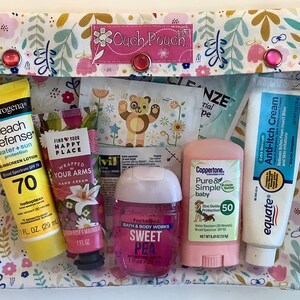 May include: A pink and white floral print pouch with a pink label that says "Ouch Pouch". The pouch contains various travel-sized toiletries, including sunscreen, hand cream, body wash, and insect repellent.