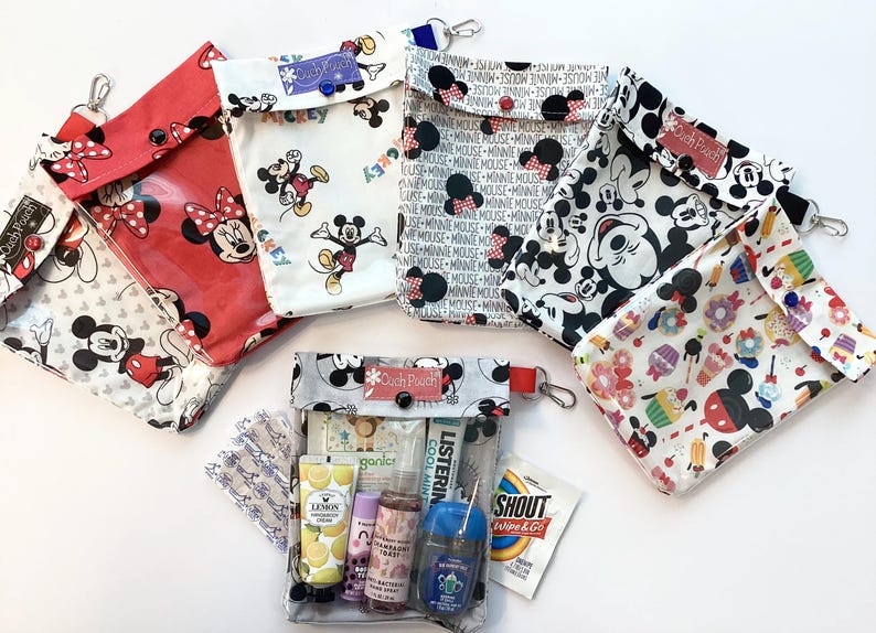 May include: A collection of Disney-themed pouches and a clear travel bag filled with toiletries. The pouches feature Mickey and Minnie Mouse designs in various colors, including red, white, and black. The clear bag contains travel-sized personal care items.