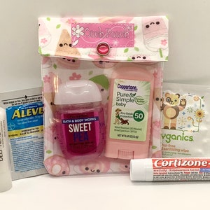 Może przedstawiać: Przezroczysty, r&oacute;żowy "Ouch Pouch" z zapięciem na zatrzask, zawierający r&oacute;żne produkty zdrowotne i kosmetyczne. Zawiera balsam do ust Blistex, środek przeciwb&oacute;lowy Aleve, środek do dezynfekcji rąk, krem ​​przeciwsłoneczny, chusteczkę dezynfekującą i krem ​​Cortizone-10.