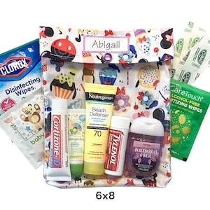 May include: A fabric pouch with a colorful dessert and character print, featuring a label that reads Abigail. It contains a Clorox wipe, a baby wipe, Cortizone-10, Babyganics cream, Neutrogena sunscreen, Tylenol, hand sanitizer, and Curad bandages.