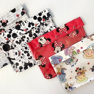 Könnte beinhalten: Vier rechteckige Beutel mit Druckknöpfen. Die Beutel weisen verschiedene Disney-Motive auf, darunter Micky Maus, Minnie Maus und Teetassen. Die Farbpalette umfasst Rot, Schwarz, Weiß und Pastelltöne.