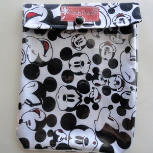 May include: A white and black pouch featuring a pattern of Mickey Mouse faces and black polka dots. The pouch has a clear front and a flap closure with a snap. The text "Cuch Pouch" is visible on a small red tag.
