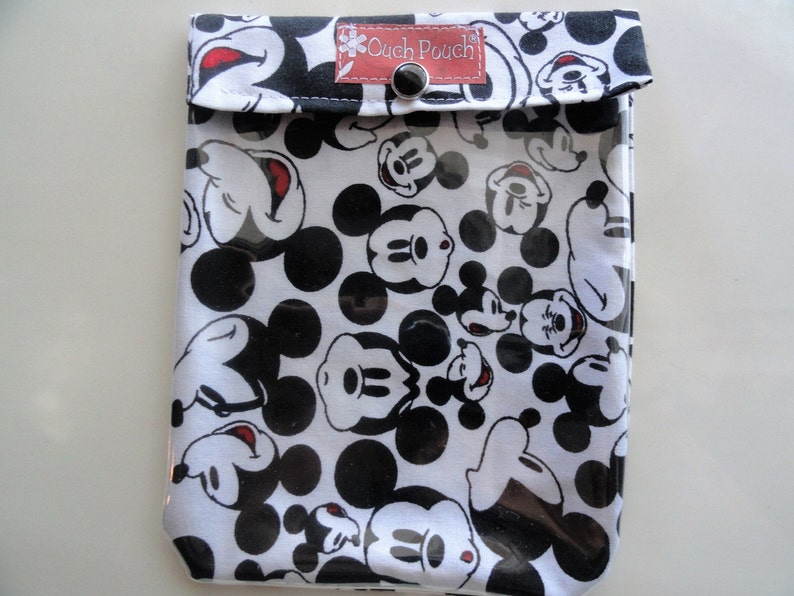 May include: A white and black pouch featuring a pattern of Mickey Mouse faces and black polka dots. The pouch has a clear front and a flap closure with a snap. The text "Cuch Pouch" is visible on a small red tag.
