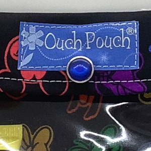May include: A black fabric pouch with a blue label that says "Ouch Pouch" and a blue button. The pouch has a colorful pattern of cartoon characters.