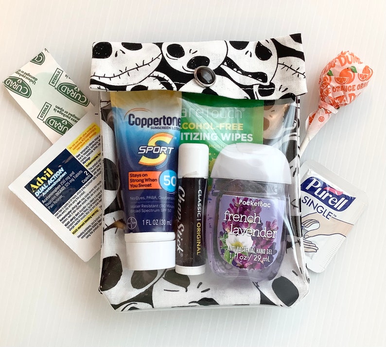 Puede incluir: Una bolsa con cremallera de patr&oacute;n blanco y negro con un frente de pl&aacute;stico transparente. La bolsa contiene varios art&iacute;culos, incluyendo protector solar, desinfectante de manos, b&aacute;lsamo labial, tabletas para el dolor y toallitas antis&eacute;pticas. La bolsa tambi&eacute;n tiene un cierre de bot&oacute;n negro.