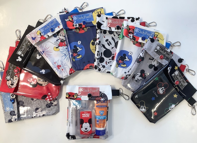 K&ouml;nnte beinhalten: Eine Sammlung von neun Rei&szlig;verschlusstaschen mit Mickey-Mouse-Motiv und durchsichtigen Plastikfenstern. Die Taschen sind aus Stoff und haben verschiedene Mickey-Mouse-Designs. Einige der Taschen haben einen Knopfverschluss. Eine Tasche hat ein durchsichtiges Plastikfenster und enth&auml;lt eine Zahnb&uuml;rste, H&auml;ndedesinfektionsmittel und Sonnencreme.