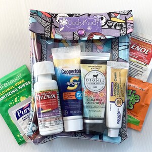 May include: A clear plastic pouch with a colorful patterned fabric exterior. The pouch contains various travel-sized toiletries, including sunscreen, hand cream, antibiotic cream, children's pain reliever, and sanitizing wipes. The pouch is labeled "Ouch Pouch".