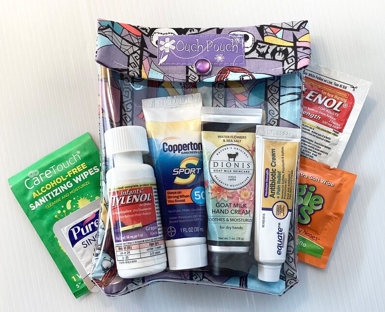 May include: A clear plastic pouch with a colorful patterned fabric exterior. The pouch contains various travel-sized toiletries, including sunscreen, hand cream, antibiotic cream, children's pain reliever, and sanitizing wipes. The pouch is labeled "Ouch Pouch".