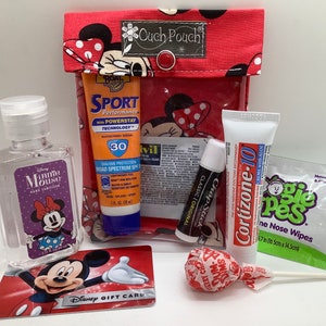 May include: A red and white Minnie Mouse themed ouch pouch with a variety of items inside, including hand sanitizer, sunscreen, lip balm, a lollipop, and a Disney gift card.