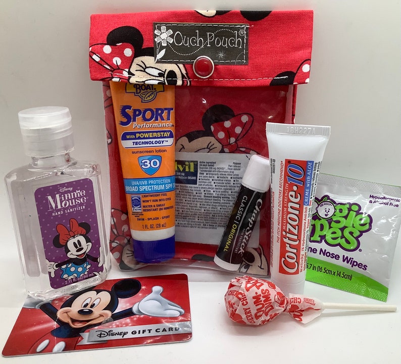 May include: A red and white Minnie Mouse themed ouch pouch with a variety of items inside, including hand sanitizer, sunscreen, lip balm, a lollipop, and a Disney gift card.