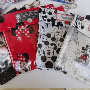 K&ouml;nnte beinhalten: Vier Rei&szlig;verschlusstaschen mit Mickey Mouse und Minnie Mouse Motiv und durchsichtigen Plastikfenstern. Die Taschen sind rot, schwarz, wei&szlig; und grau mit wei&szlig;en Punkten. Die Taschen haben einen Metallverschluss und ein Etikett mit den Namen "Jessie", "Ouch Pouch", "Bonnie" und "Suzy".