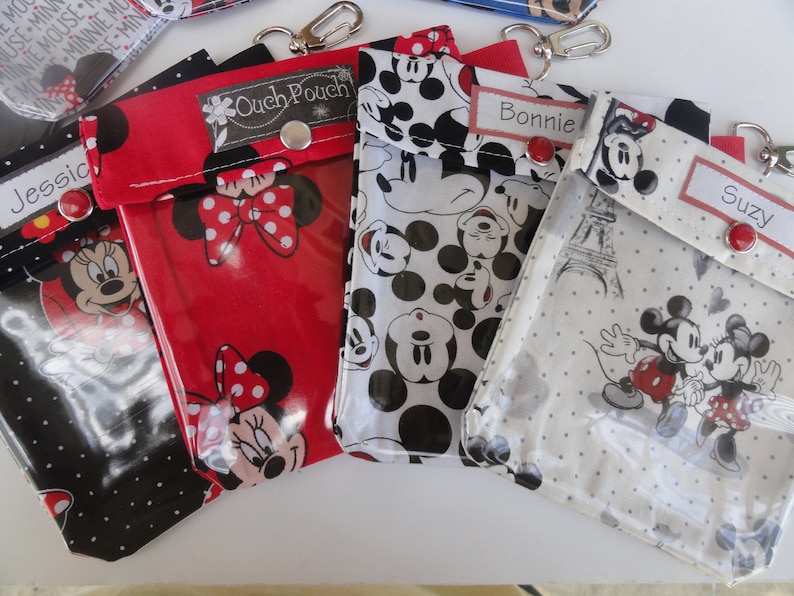 K&ouml;nnte beinhalten: Vier Rei&szlig;verschlusstaschen mit Mickey Mouse und Minnie Mouse Motiv und durchsichtigen Plastikfenstern. Die Taschen sind rot, schwarz, wei&szlig; und grau mit wei&szlig;en Punkten. Die Taschen haben einen Metallverschluss und ein Etikett mit den Namen "Jessie", "Ouch Pouch", "Bonnie" und "Suzy".