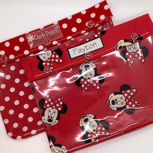 May include: Two red and white polka dot fabric pouches with clear vinyl fronts. The pouches have a Minnie Mouse print and the name "Payton" is written on one of the pouches.