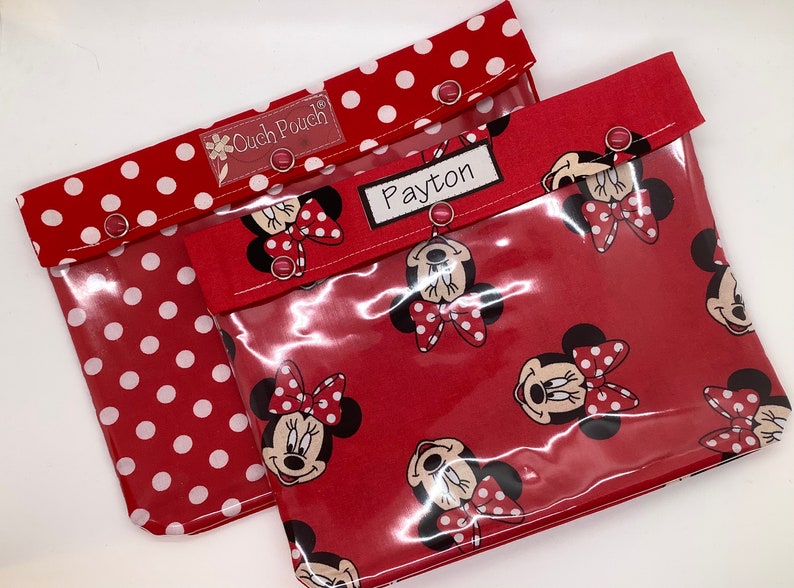 May include: Two red and white polka dot fabric pouches with clear vinyl fronts. The pouches have a Minnie Mouse print and the name "Payton" is written on one of the pouches.