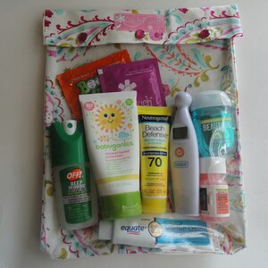 May include: A floral patterned pouch labeled "Couch Pouch" containing various travel-sized toiletries. Items include sunscreen, insect repellent, hand sanitizer, and a thermometer. The pouch is closed with two red snap closures.