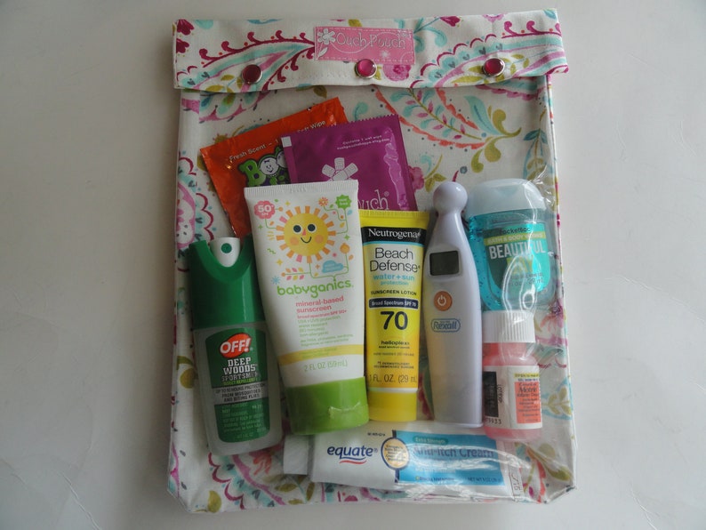 May include: A floral patterned pouch labeled "Couch Pouch" containing various travel-sized toiletries. Items include sunscreen, insect repellent, hand sanitizer, and a thermometer. The pouch is closed with two red snap closures.