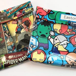 May include: Two rectangular pouches. One features comic book panels with the Hulk and Spider-Man. The other has cartoon superhero characters. Both have a clear front, snap closures, and the text "Ouch Pouch" and "Easton".