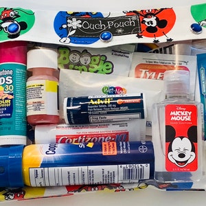 Puede incluir: Una bolsa de tela blanca con estampado de Mickey Mouse, que contiene varios artículos de primeros auxilios. Incluye protector solar, desinfectante de manos, Advil y crema de hidrocortisona. La bolsa está etiquetada como "Ouch Pouch" y tiene cierres de botón azules.