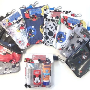 Könnte beinhalten: Verschiedene Disney-Pouches mit Mickey Mouse-Designs. Die farbenfrohen Pouches, in Rot, Blau, Schwarz und Grau, tragen den Schriftzug "Ouch Pouch". Einige haben eine transparente Vorderseite.