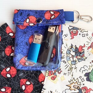 May include: A blue fabric pouch with a zipper closure and a silver key ring. The pouch has a Spiderman design and is filled with two USB drives.