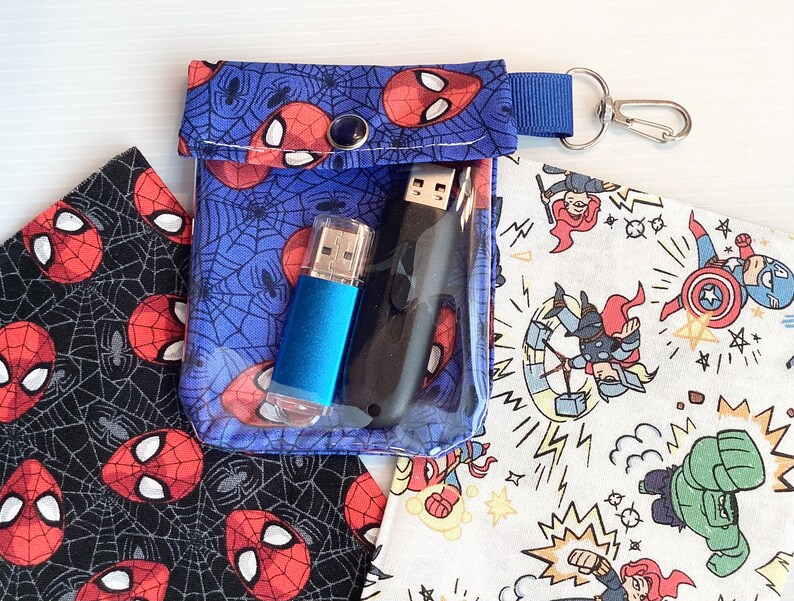 May include: A blue fabric pouch with a zipper closure and a silver key ring. The pouch has a Spiderman design and is filled with two USB drives.