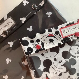 May include: Two black and white Mickey Mouse fabric pouches with clear vinyl front panels. Each pouch has a black label with white text that reads "E. Hernandez". The pouches have red buttons.