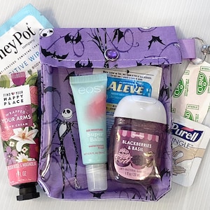 Puede incluir: Una bolsa de cremallera morada con un dise&ntilde;o de Pesadilla Antes de Navidad. La bolsa contiene varios art&iacute;culos, incluyendo crema de manos, b&aacute;lsamo labial, desinfectante de manos y una tirita. La bolsa tiene un peque&ntilde;o bot&oacute;n morado y un llavero plateado.