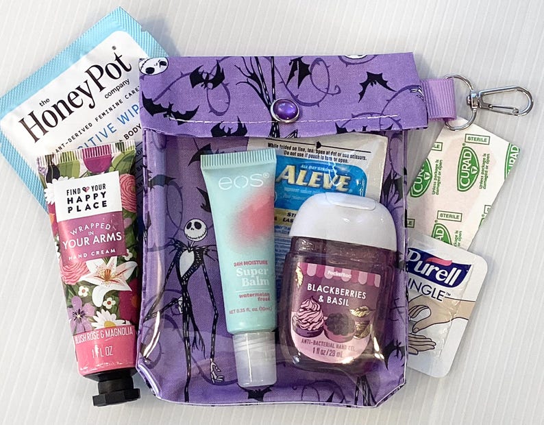 Puede incluir: Una bolsa de cremallera morada con un dise&ntilde;o de Pesadilla Antes de Navidad. La bolsa contiene varios art&iacute;culos, incluyendo crema de manos, b&aacute;lsamo labial, desinfectante de manos y una tirita. La bolsa tiene un peque&ntilde;o bot&oacute;n morado y un llavero plateado.