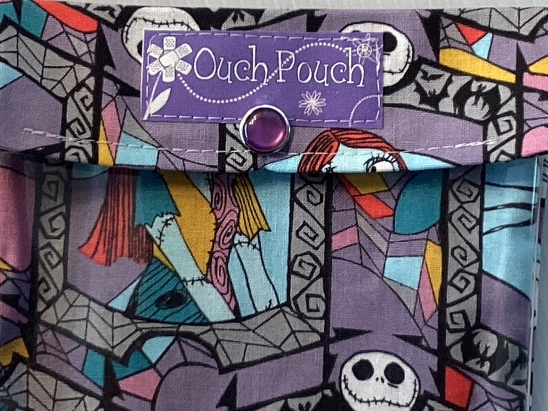 May include: A purple fabric pouch with a Nightmare Before Christmas print. The pouch has a purple label that says "Ouch-Pouch" and a purple button.