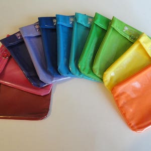 May include: A set of ten clear plastic pouches with zipper closures. The pouches are arranged in a rainbow pattern, with the colors red, orange, yellow, green, blue, indigo, and violet. The pouches are labeled with the text "Coach Pouch".