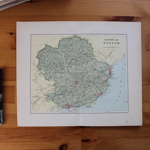 Op de afbeelding: Een vintage kaart van het graafschap Forfar, Schotland, met gedetailleerde geografische kenmerken in groen, rood en blauw. De kaart is wit omlijst en ligt op een houten oppervlak, naast een zwarte pen.