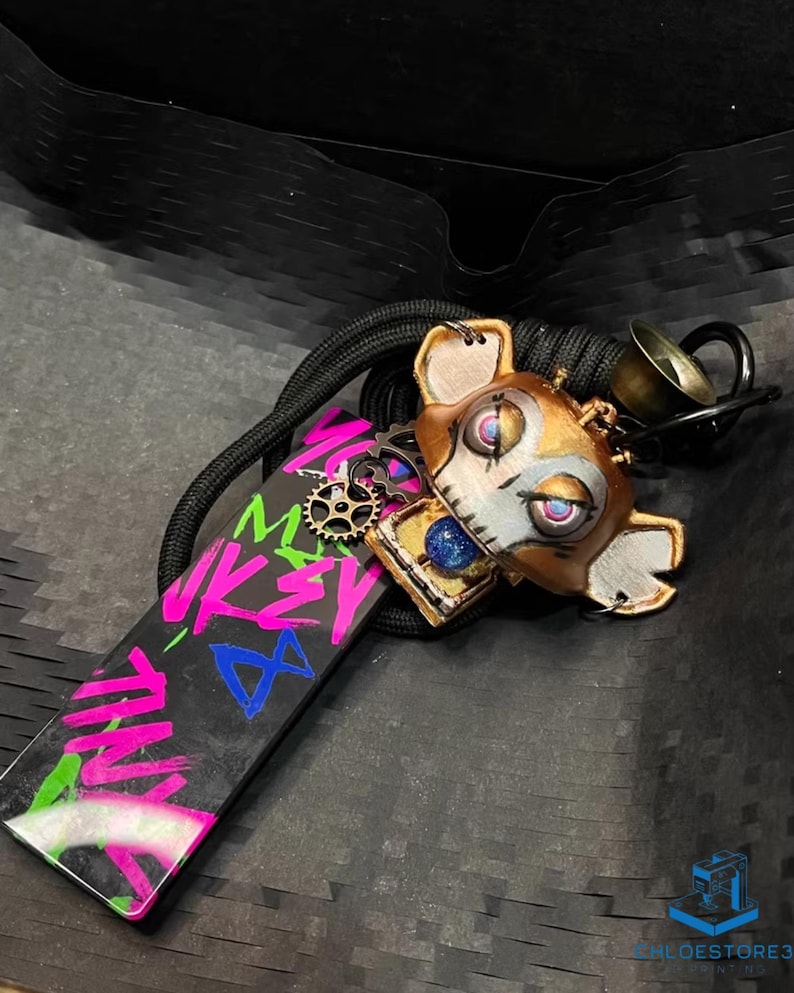 May include: A black and white keychain with a pink, blue, and green graphic that says "Mikey Mouse". The keychain also features a brown, white, and blue robot-like figure with a gear on its chest.