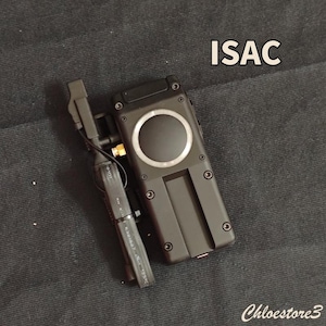 Puede incluir: Dispositivo electr&oacute;nico negro con un dise&ntilde;o circular y la palabra "ISAC" en blanco. El dispositivo tiene forma rectangular con varios tornillos y un componente m&aacute;s peque&ntilde;o adjunto. La imagen est&aacute; sobre una superficie gris oscuro.