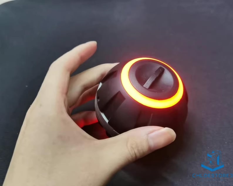 May include: A black and orange round speaker with a glowing orange ring around the top. The speaker is being held in a hand.