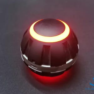 May include: A black and silver round object with a glowing orange ring around the top and a red light emanating from the bottom.
